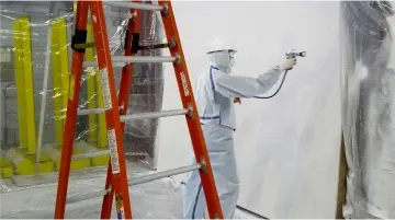 An applicator is spaying intumescent paint on gypsum